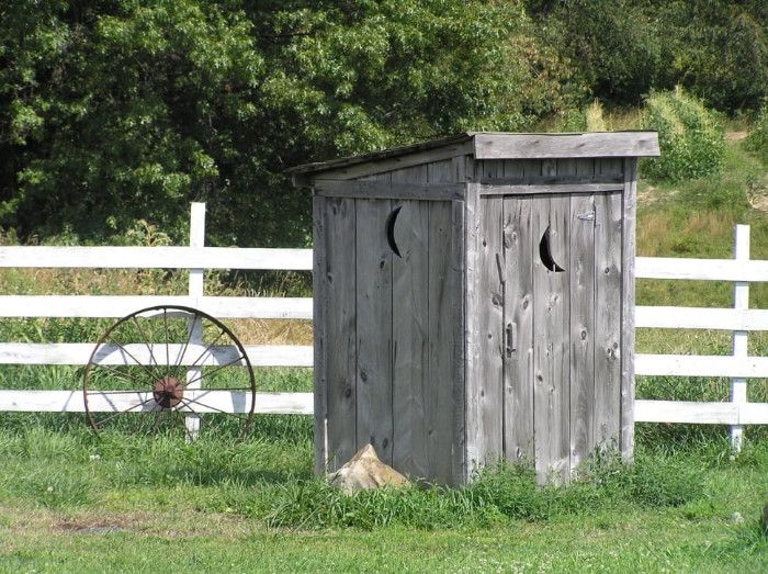 Outhouse in a field, in front of fence